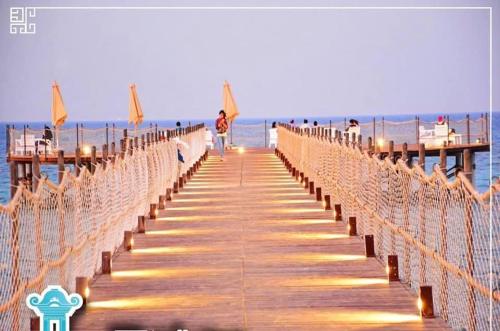 a wooden boardwalk leading to the beach at dusk at blue bay sokhna aqua park - مارسيليا بلو باى السخنه -عائلات فقط in Ain Sokhna