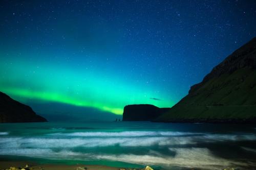 an aurora over a body of water at night at Luxurious & Unique Villa / Nature / Beach / Hiking in Tjørnuvík