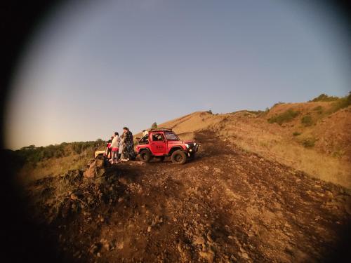 a group of people standing around a red jeep on a dirt road at Batur lake view in Kintamani