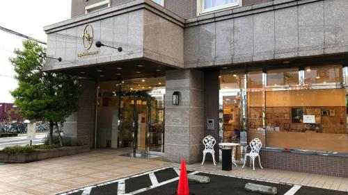 Toyoko Inn Aizuwakamatsu Ekimae في أيزواكاماتسو: مبنى امامه كرسيين وطاولة
