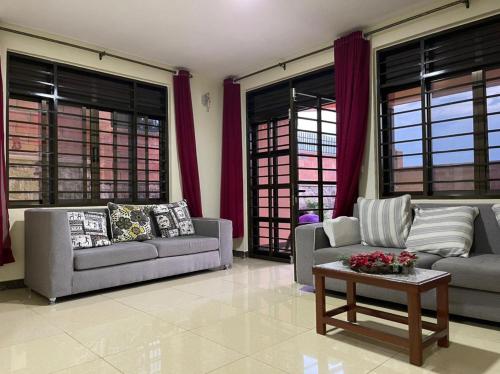 a living room with couches and a table and windows at The Mugabis Spacious Private Room in Kigali