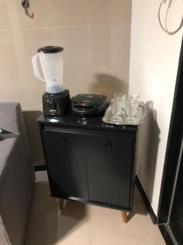 ein Mixer auf einem schwarzen Ständer mit Tassen und Geschirr in der Unterkunft Flat Aju - Um jeitinho especial de se hospedar em Aracaju. Uma verdadeira suíte master todo mobiliado no capricho só para você. in Aracaju