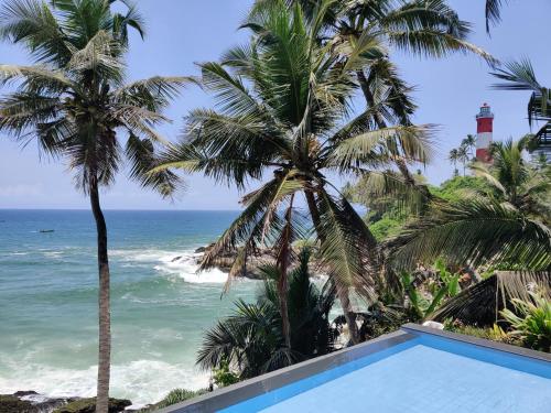 a swimming pool with palm trees and the ocean at Rockholm at the Light House Beach in Kovalam