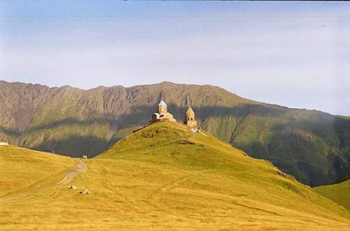 a building on top of a hill with mountains in the background at Crystal Kazbegi in Kazbegi