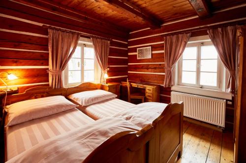two beds in a room with wooden walls and windows at Panský dům - Jizerka in Jizerka