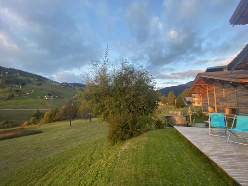a wooden deck next to a house with a field at La Ferme des Georgières "Séjour en tout compris" in Notre-Dame-de-Bellecombe