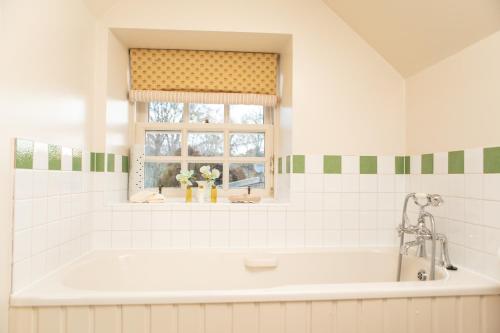 baño con bañera blanca y ventana en Balnagown Estates Gardener's Cottage, en Kildary
