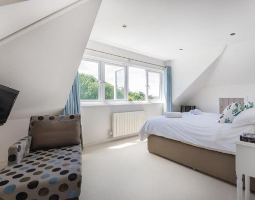 a white bedroom with a bed and a chair at The Wrens in Polzeath