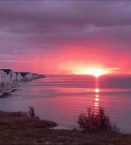 a sunset over a body of water with the sun setting at Gîte des falaises in Ault