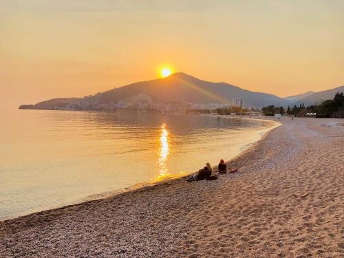 two people sitting on the beach watching the sunset at Apartment "Gluecks-Griff" inside "Becici Sunset Apartments" in Budva