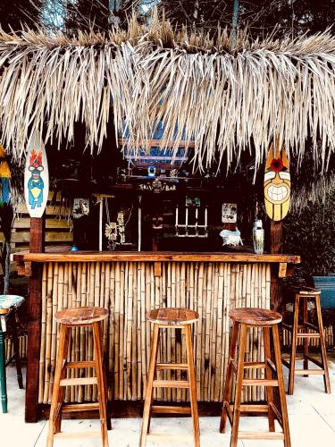a bar with four wooden stools and a straw umbrella at Airstream Woodland Escape in Galston
