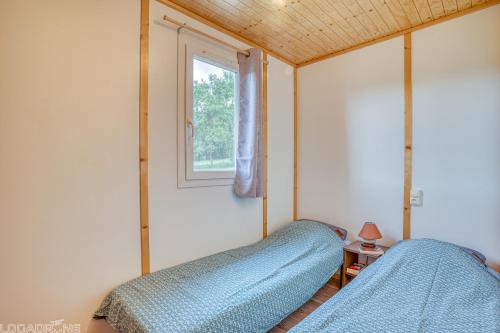2 letti in una piccola camera con finestra di Les chalets de Dordogne a Razac-dʼEymet