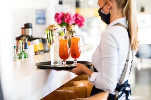 a woman in a mask holding a tray with two drinks at Hôtel & Spa Villa Seren in Hossegor