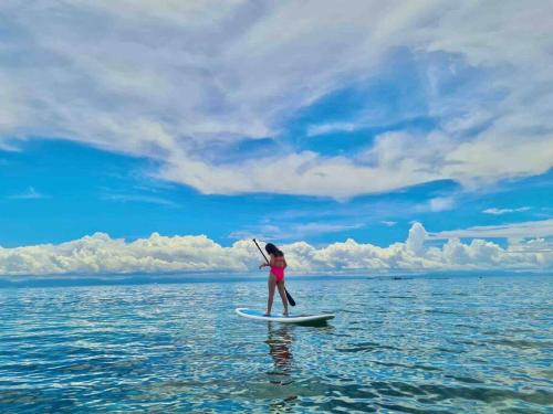 a woman standing on a surfboard in the ocean at Toliz Beach House -Sipaway Island San Carlos City in San Juan
