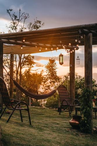 a hammock and chairs under a pergola with the sunset at Chalé Refugio da Pedra SP in São Bento do Sapucaí