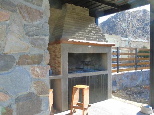 un horno de piedra con un taburete de madera delante de él en Base Manzano en Tunuyán