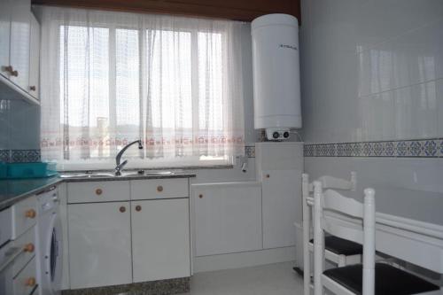 uma cozinha com armários brancos, um lavatório e uma janela em Precioso apartamento de 3 habitaciones en Cabañas. em Cabanas