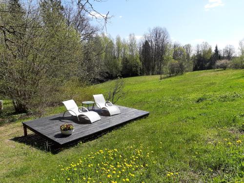 two white chairs sitting on a table in a field at Mošķu Pirts meža māja in Turaida