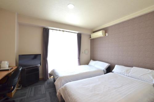a hotel room with two beds and a television at New Station Hotel in Isahaya