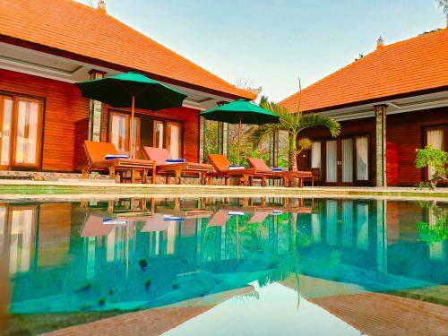 a house with chairs and umbrellas next to a swimming pool at Juan Beach Bungalow in Nusa Penida