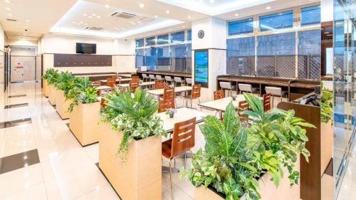 eine Cafeteria mit Tischen, Stühlen und Pflanzen in der Unterkunft Toyoko Inn Hiroshima-eki Shinkansen-guchi No.2 in Hiroshima