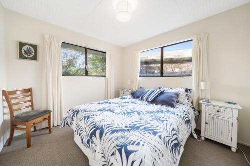 a bedroom with a bed and a chair and windows at Babbacombe Bach - Otaki Beach Holiday Home in Otaki Beach