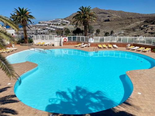 a large blue swimming pool with palm trees and mountains at Casa Aita - refurbished apartment with unparalleled sea view in Mogán