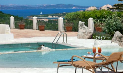 2 Stühle und ein Tisch neben einem Pool in der Unterkunft Hotel Pulicinu in Baja Sardinia