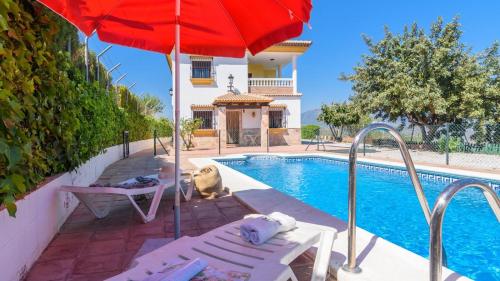 a pool with a red umbrella and chairs next to a house at Casa Casana Almáchar by Ruralidays in Almáchar