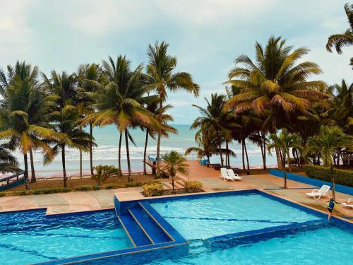 a swimming pool next to a beach with palm trees at Playa Azul Suites in Tonsupa