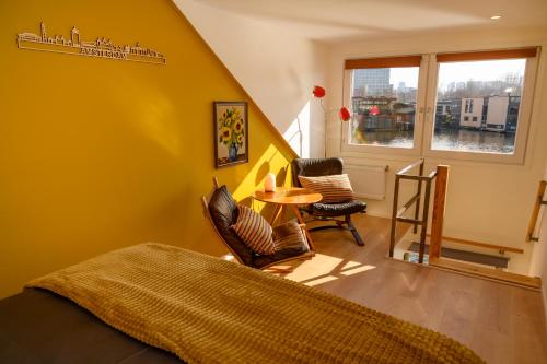 Houseboat studio with canalview and free bikes في أمستردام: غرفة نوم بجدران صفراء وطاولة وكراسي