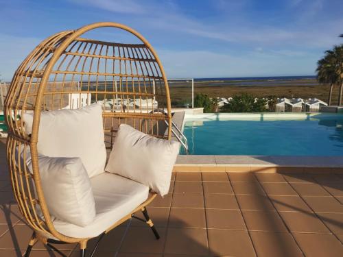 a rattan chair with white pillows sitting on a patio at Casa Figueira by Portucasa in Fuzeta