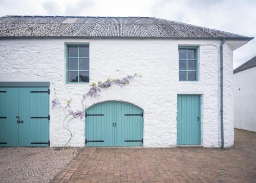 a white building with two green garage doors at Coachmans Bothy - 50m from the beach in Port Appin