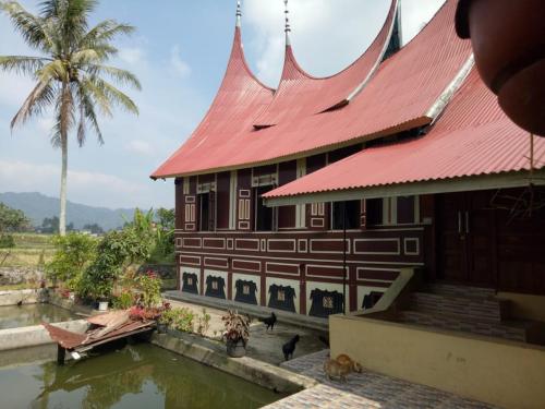 un edificio con tetto rosso accanto a un corpo d'acqua di Rumah Gadang Simarasok a Baso
