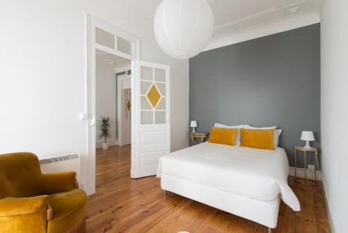 een slaapkamer met een wit bed met oranje kussens en een stoel bij CASASUPERTUBOS® Apart 9-14 in Peniche