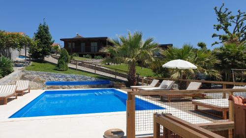 a pool with chairs and an umbrella next to a house at Quintinha do Periqueiro in Castelo do Neiva