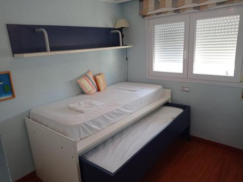 małe łóżko w pokoju z 2 oknami w obiekcie Bahamas II Solo Familias Serviplaya w mieście Playa de Gandia