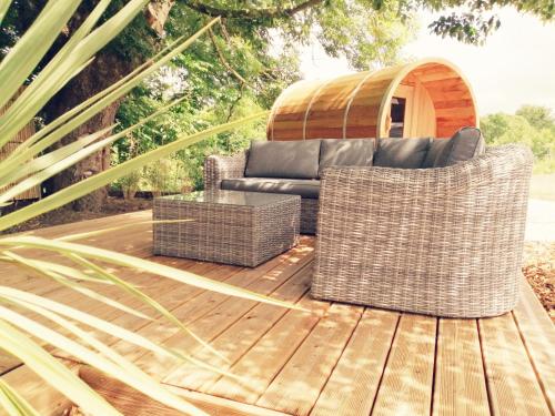 un sofá y 2 sillas de mimbre en una terraza de madera en Le Domaine de Pivette Chambre climatisée et insolite avec terrasse privative, en Avranches