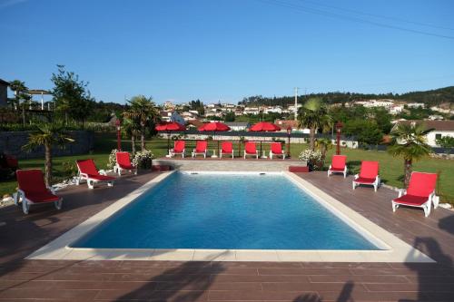 a swimming pool with red chairs and a group of tables at Aldeia da Quinta do Paço - Turismo rural Santo Tirso in Santo Tirso