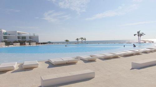 a swimming pool with white lounge chairs and the ocean at Amazing &Totally New!!! Aria Ocean Condo 306 by Kivoya in Nuevo Vallarta