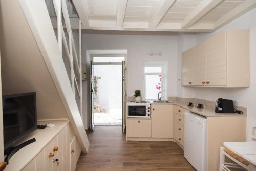 a kitchen with white cabinets and a television and a staircase at Myconian Old Town Maisonette THE MIMIs PLACE in Mikonos