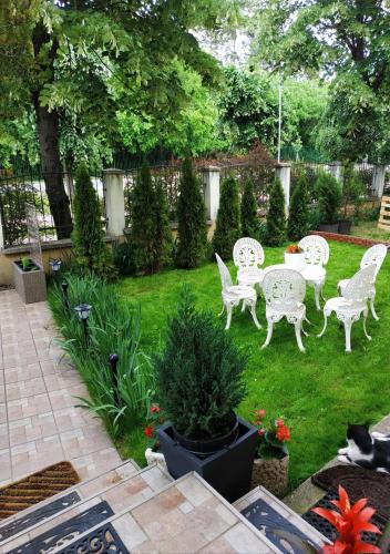 a patio with white chairs and a table in a yard at Wagner Apartman Tata in Tata