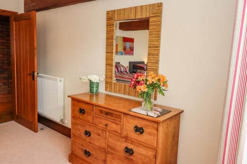 a vase of flowers on a dresser with a mirror at Cartwheels Cottage in Great Driffield