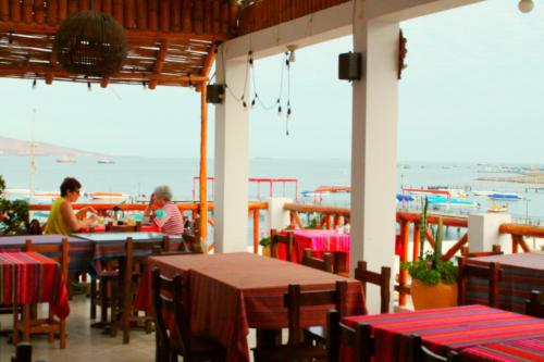 two people sitting at tables in a restaurant with a view of the ocean at El Gamonal - Paracas in Paracas