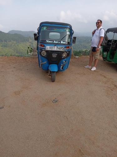 a man standing next to a blue motor bike on a dirt road at Barn Hills in Ella