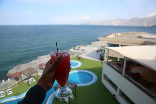 a person holding a drink with a view of the ocean at Atana Khasab Hotel in Khasab