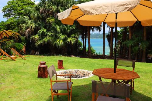 a table and chairs with an umbrella and a fire place at 泊まれるアートミュージアム 琉球ヴィラ in Tatsugo