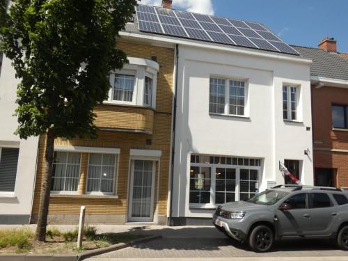 une voiture garée devant une maison avec des panneaux solaires sur le toit dans l'établissement B&B De Noorderwind, à Schoonaarde