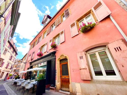 a pink building with tables and chairs on a street at Le Schongauer in Colmar