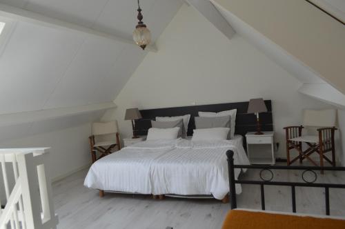 a white bedroom with a large white bed and chairs at Huis aan Honte in Dishoek